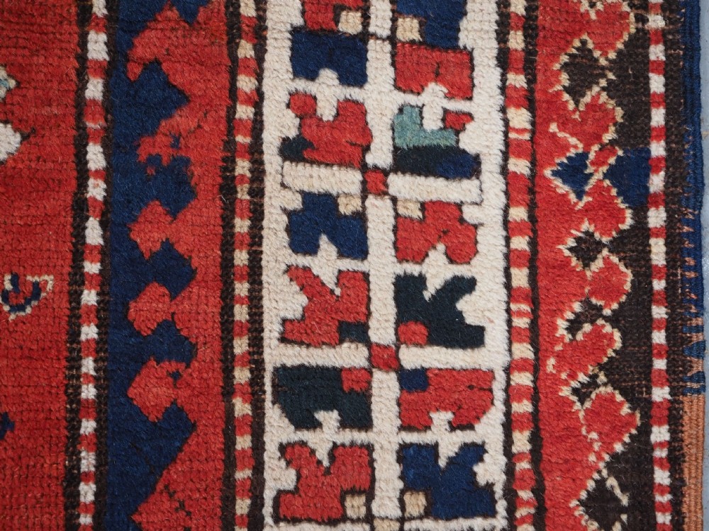 An antique Caucasian Bordjalou Kazak hand-knotted wool rug featuring three stepped geometric medallions on a vibrant red field within patterned borders. View XI