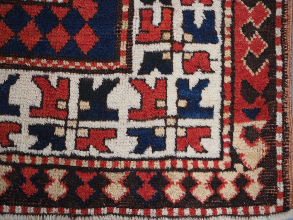 An antique Caucasian Bordjalou Kazak hand-knotted wool rug featuring three stepped geometric medallions on a vibrant red field within patterned borders. View XII