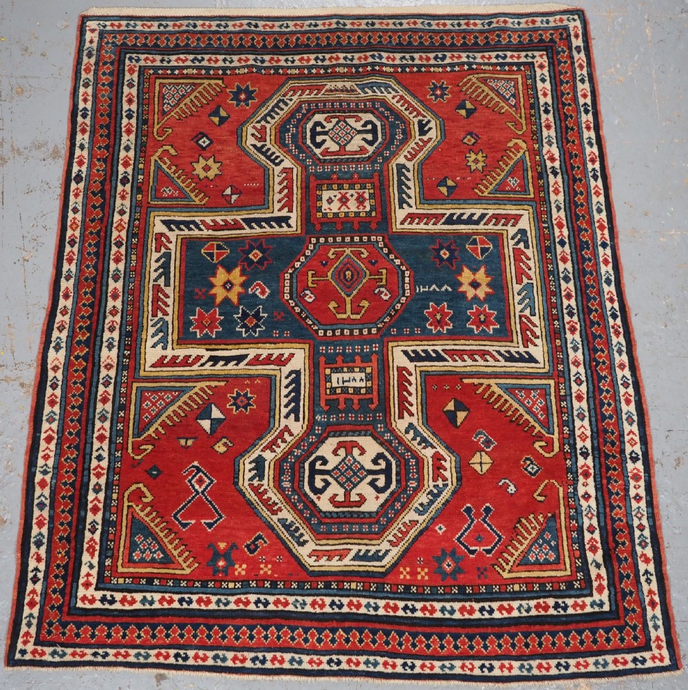 An antique Caucasian Sewan Kazak wool rug featuring a red keyhole medallion set against a navy blue and cream background with geometric borders.