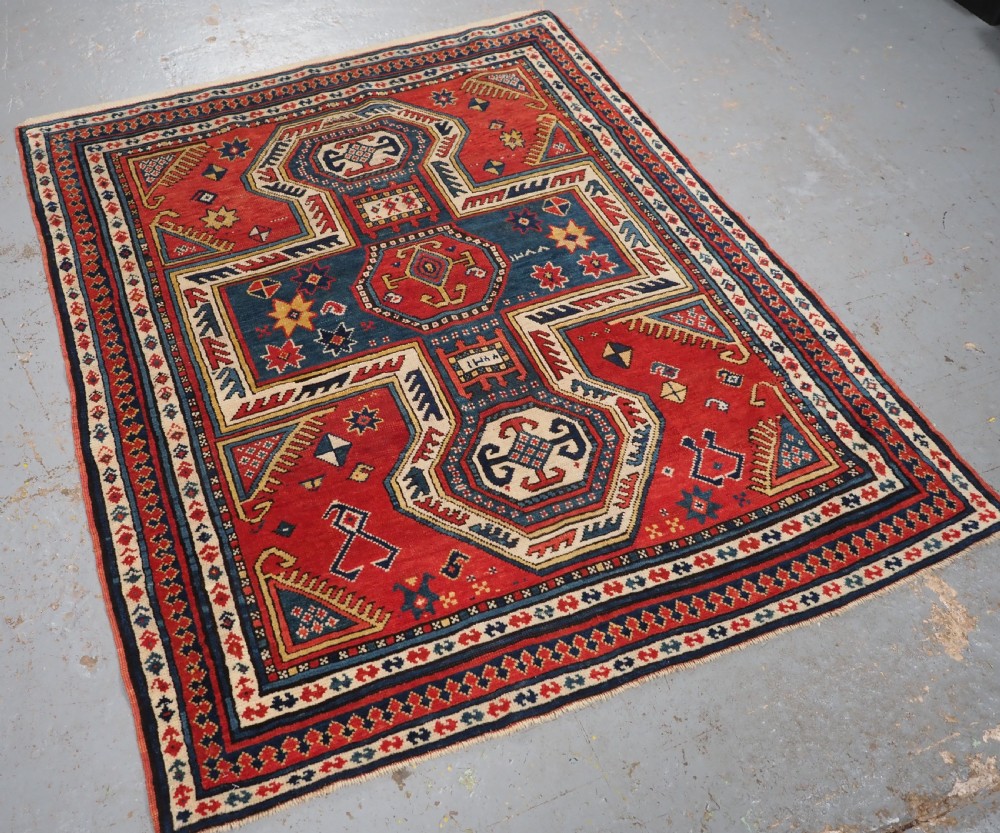 An antique Caucasian Sewan Kazak wool rug featuring a red keyhole medallion set against a navy blue and cream background with geometric borders. View II