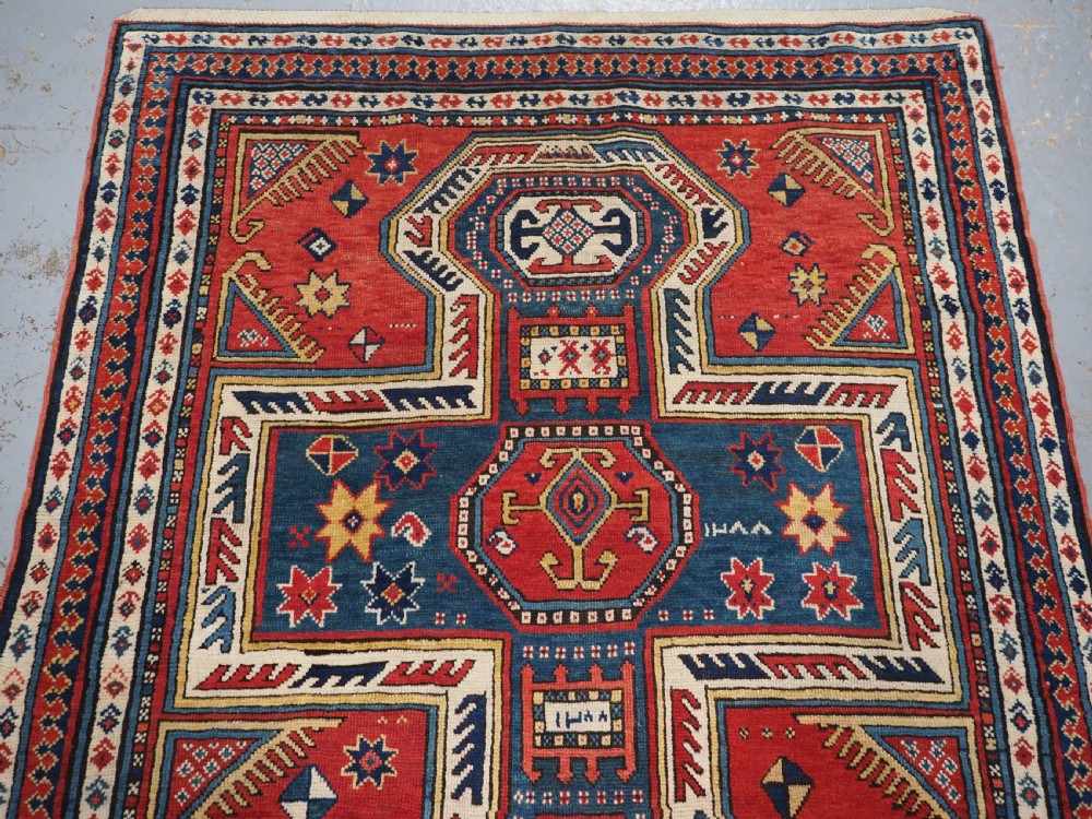 An antique Caucasian Sewan Kazak wool rug featuring a red keyhole medallion set against a navy blue and cream background with geometric borders. View III