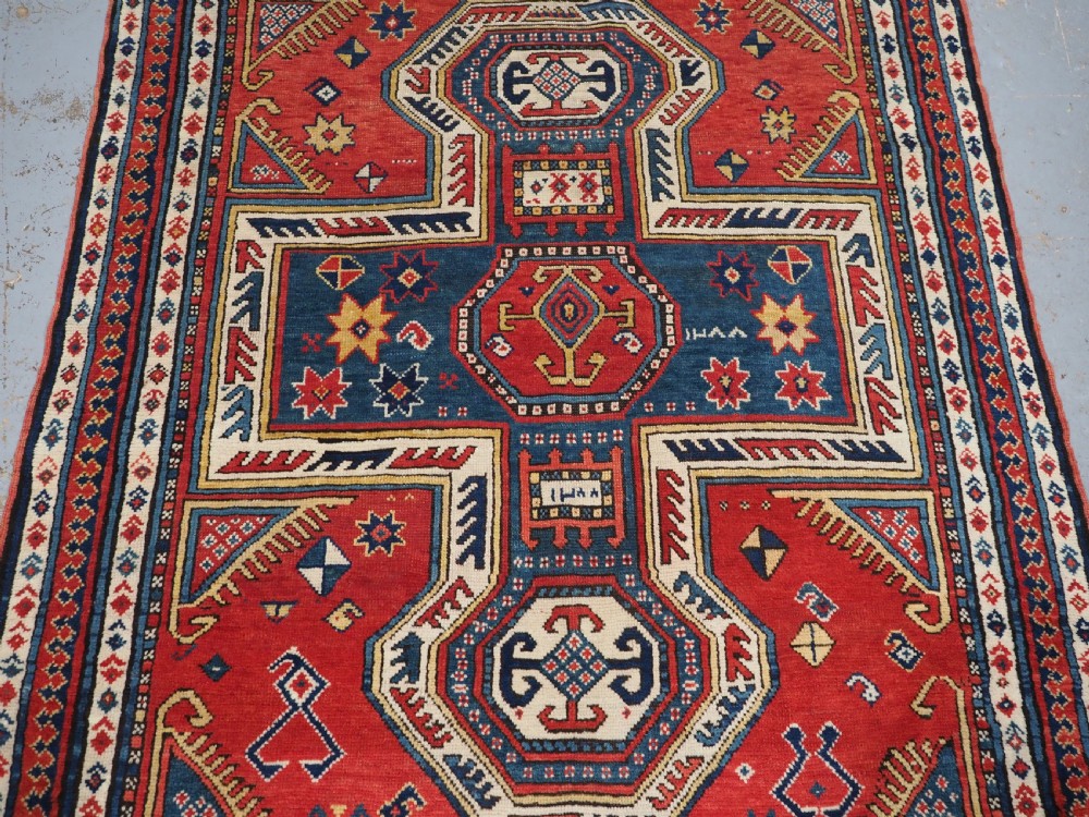 An antique Caucasian Sewan Kazak wool rug featuring a red keyhole medallion set against a navy blue and cream background with geometric borders. View IV