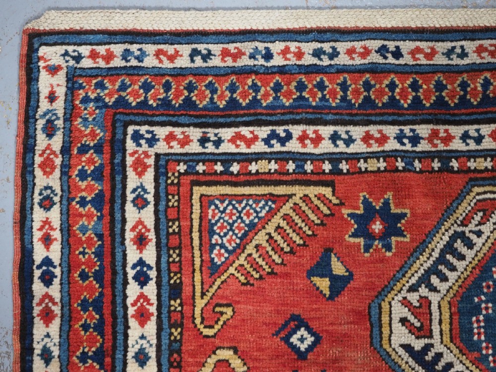 An antique Caucasian Sewan Kazak wool rug featuring a red keyhole medallion set against a navy blue and cream background with geometric borders. View VI