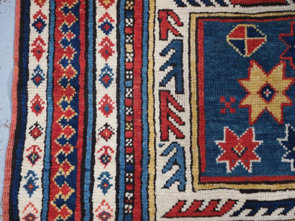An antique Caucasian Sewan Kazak wool rug featuring a red keyhole medallion set against a navy blue and cream background with geometric borders. View VII