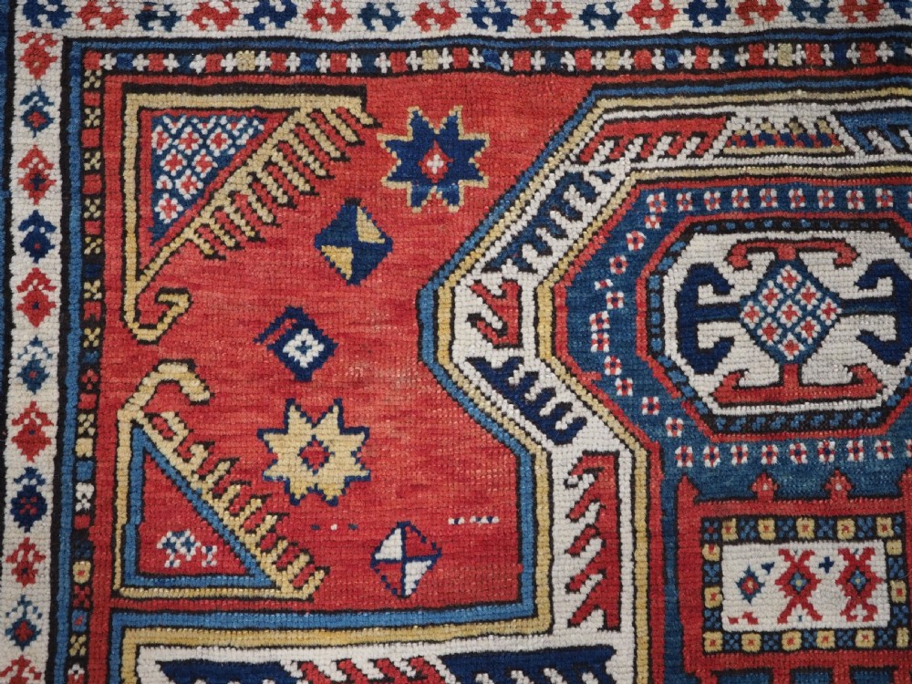 An antique Caucasian Sewan Kazak wool rug featuring a red keyhole medallion set against a navy blue and cream background with geometric borders. View VIII