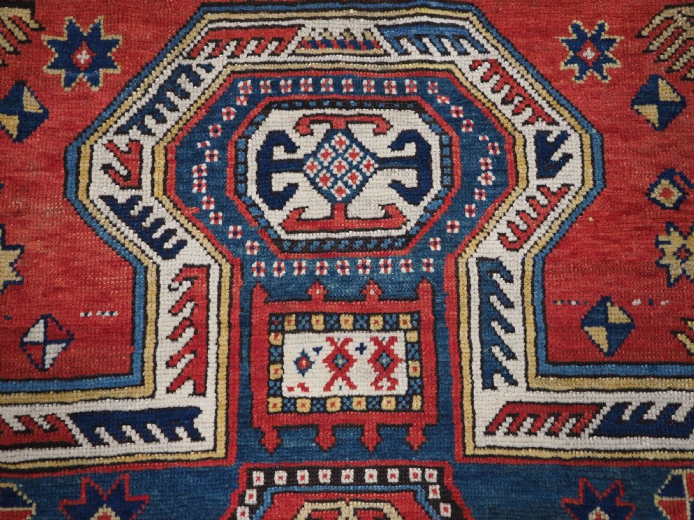 An antique Caucasian Sewan Kazak wool rug featuring a red keyhole medallion set against a navy blue and cream background with geometric borders. View IX