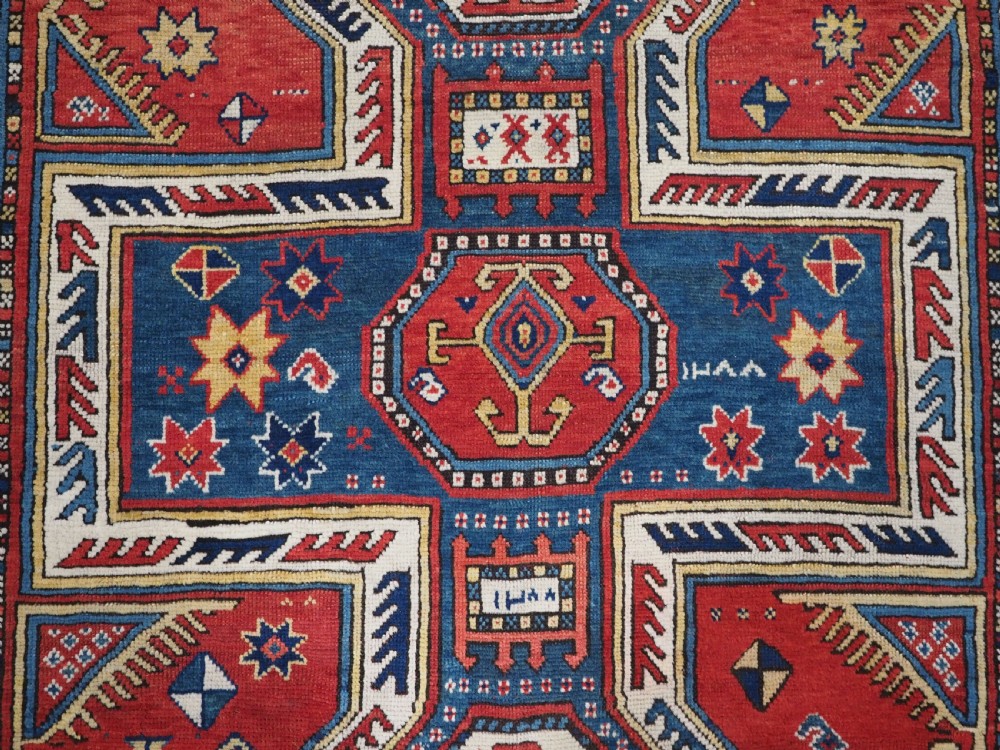 An antique Caucasian Sewan Kazak wool rug featuring a red keyhole medallion set against a navy blue and cream background with geometric borders. View X
