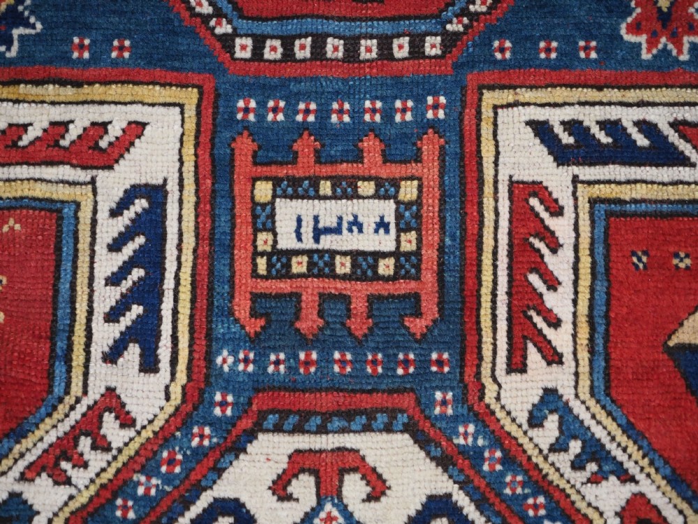 An antique Caucasian Sewan Kazak wool rug featuring a red keyhole medallion set against a navy blue and cream background with geometric borders. View XIV