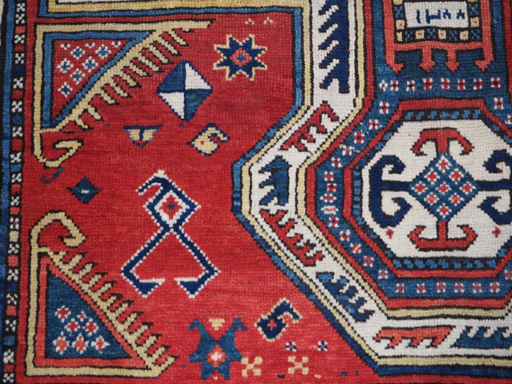 An antique Caucasian Sewan Kazak wool rug featuring a red keyhole medallion set against a navy blue and cream background with geometric borders. View XV