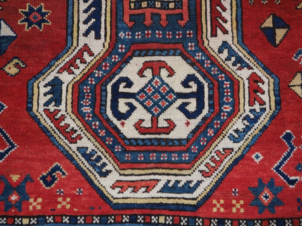 An antique Caucasian Sewan Kazak wool rug featuring a red keyhole medallion set against a navy blue and cream background with geometric borders. View XVI