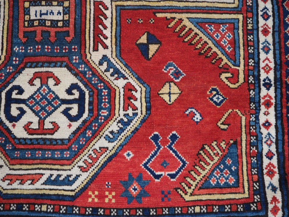 An antique Caucasian Sewan Kazak wool rug featuring a red keyhole medallion set against a navy blue and cream background with geometric borders. View XVII