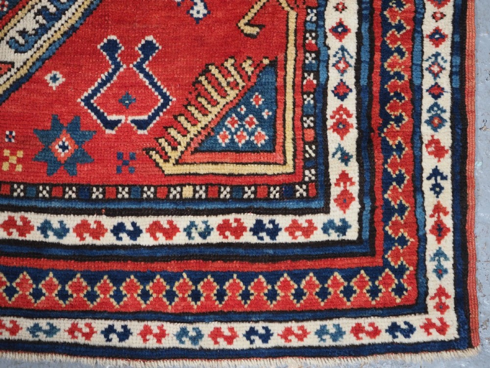 An antique Caucasian Sewan Kazak wool rug featuring a red keyhole medallion set against a navy blue and cream background with geometric borders. View XVIII