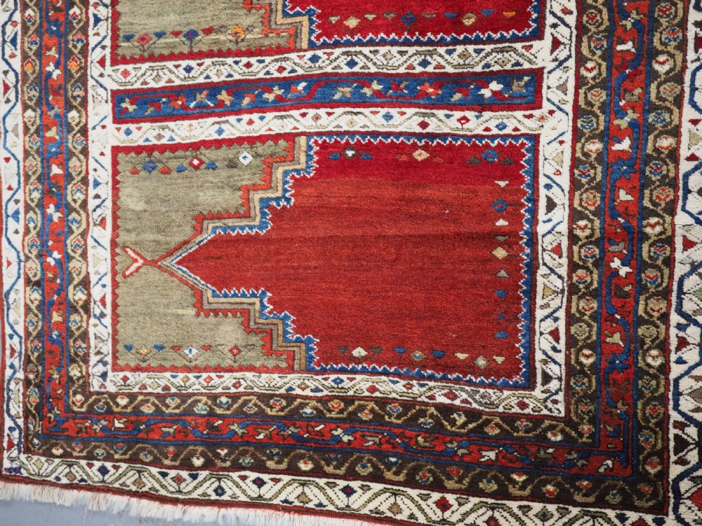 An antique Turkish Sivas Saf hand-knotted wool rug featuring three distinct red stepped prayer niches framed by olive green panels and multi-layered geometric borders. View II