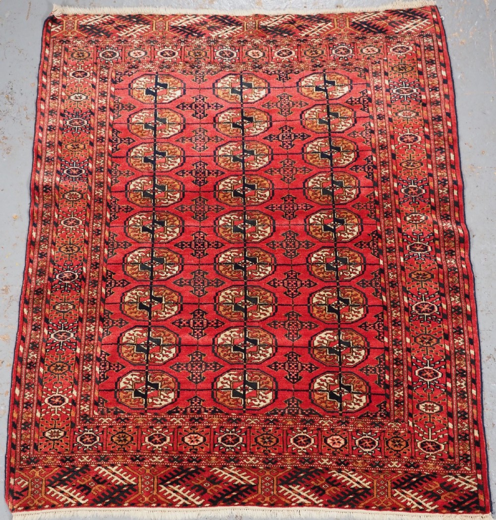 An antique Tekke Turkmen hand-woven wool rug featuring repeating octagonal gol motifs on a deep red field surrounded by geometric borders.