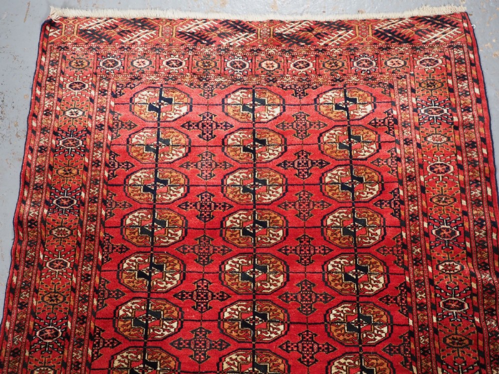 An antique Tekke Turkmen hand-woven wool rug featuring repeating octagonal gol motifs on a deep red field surrounded by geometric borders. View III