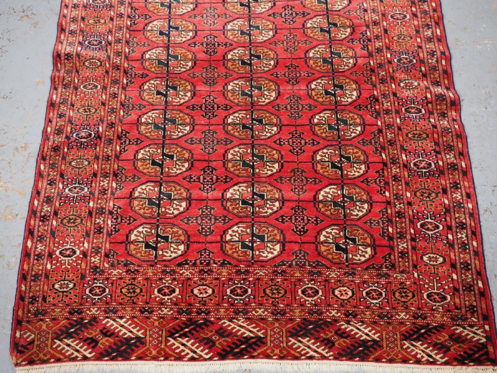 An antique Tekke Turkmen hand-woven wool rug featuring repeating octagonal gol motifs on a deep red field surrounded by geometric borders. View IV