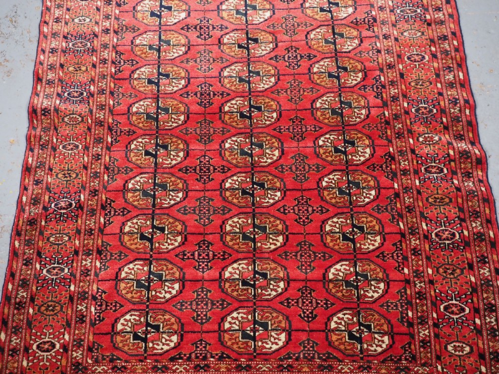 An antique Tekke Turkmen hand-woven wool rug featuring repeating octagonal gol motifs on a deep red field surrounded by geometric borders. View V