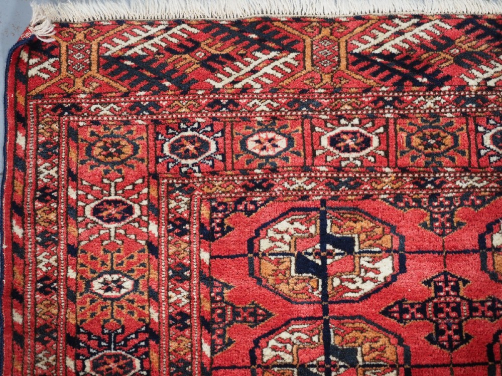 An antique Tekke Turkmen hand-woven wool rug featuring repeating octagonal gol motifs on a deep red field surrounded by geometric borders. View VI