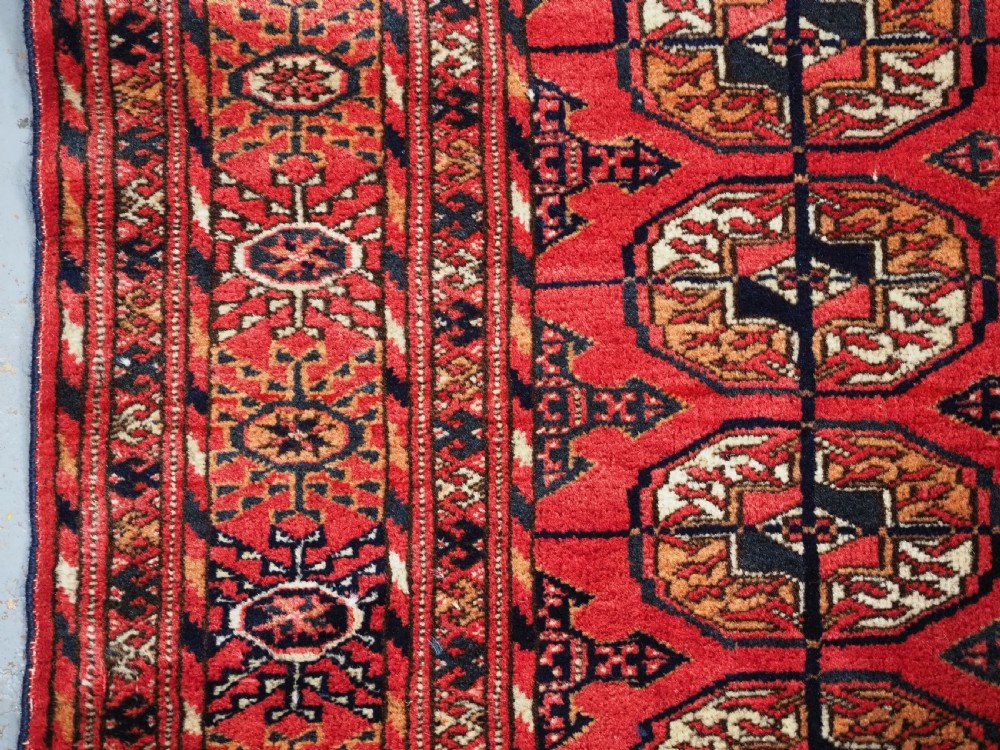 An antique Tekke Turkmen hand-woven wool rug featuring repeating octagonal gol motifs on a deep red field surrounded by geometric borders. View VII