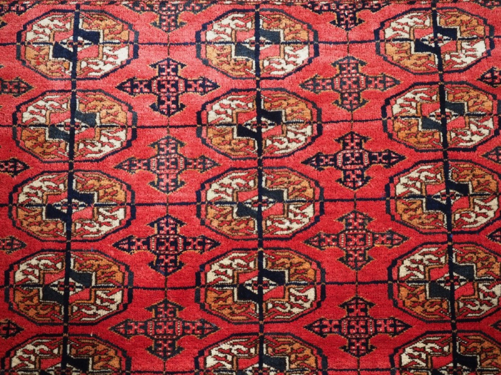 An antique Tekke Turkmen hand-woven wool rug featuring repeating octagonal gol motifs on a deep red field surrounded by geometric borders. View VIII