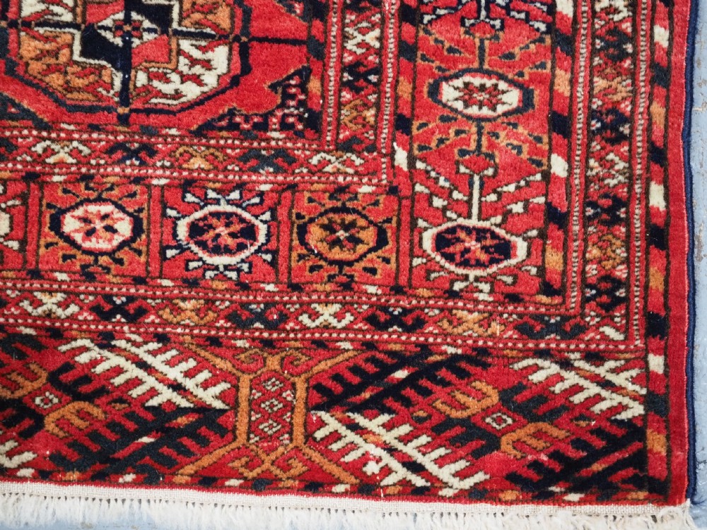 An antique Tekke Turkmen hand-woven wool rug featuring repeating octagonal gol motifs on a deep red field surrounded by geometric borders. View IX