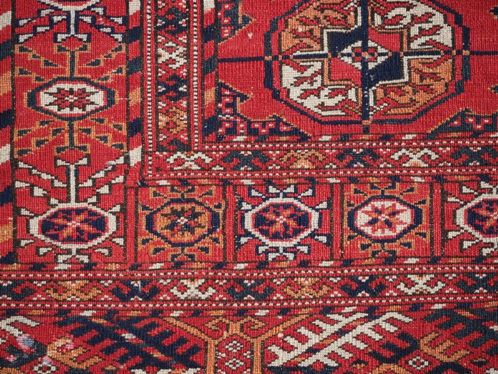 An antique Tekke Turkmen hand-woven wool rug featuring repeating octagonal gol motifs on a deep red field surrounded by geometric borders. View X