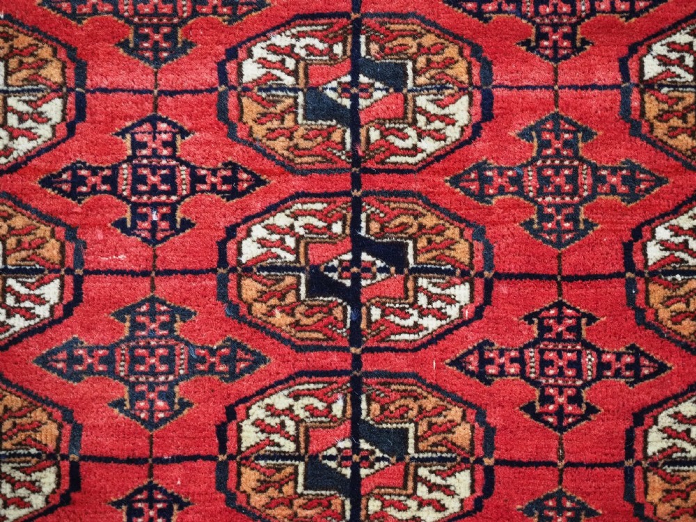 An antique Tekke Turkmen hand-woven wool rug featuring repeating octagonal gol motifs on a deep red field surrounded by geometric borders. View XI