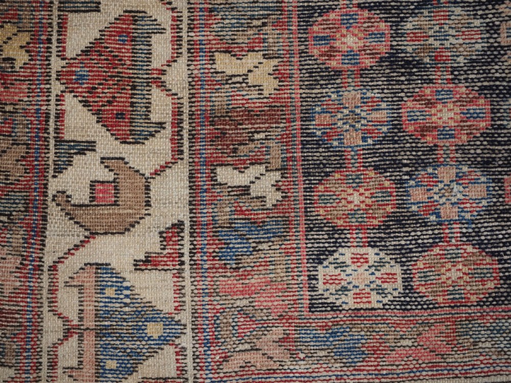 An antique hand-knotted Persian Mazlaghan wool rug featuring a central camel-coloured medallion on a red stepped field with dark blue rosette borders. View VIII