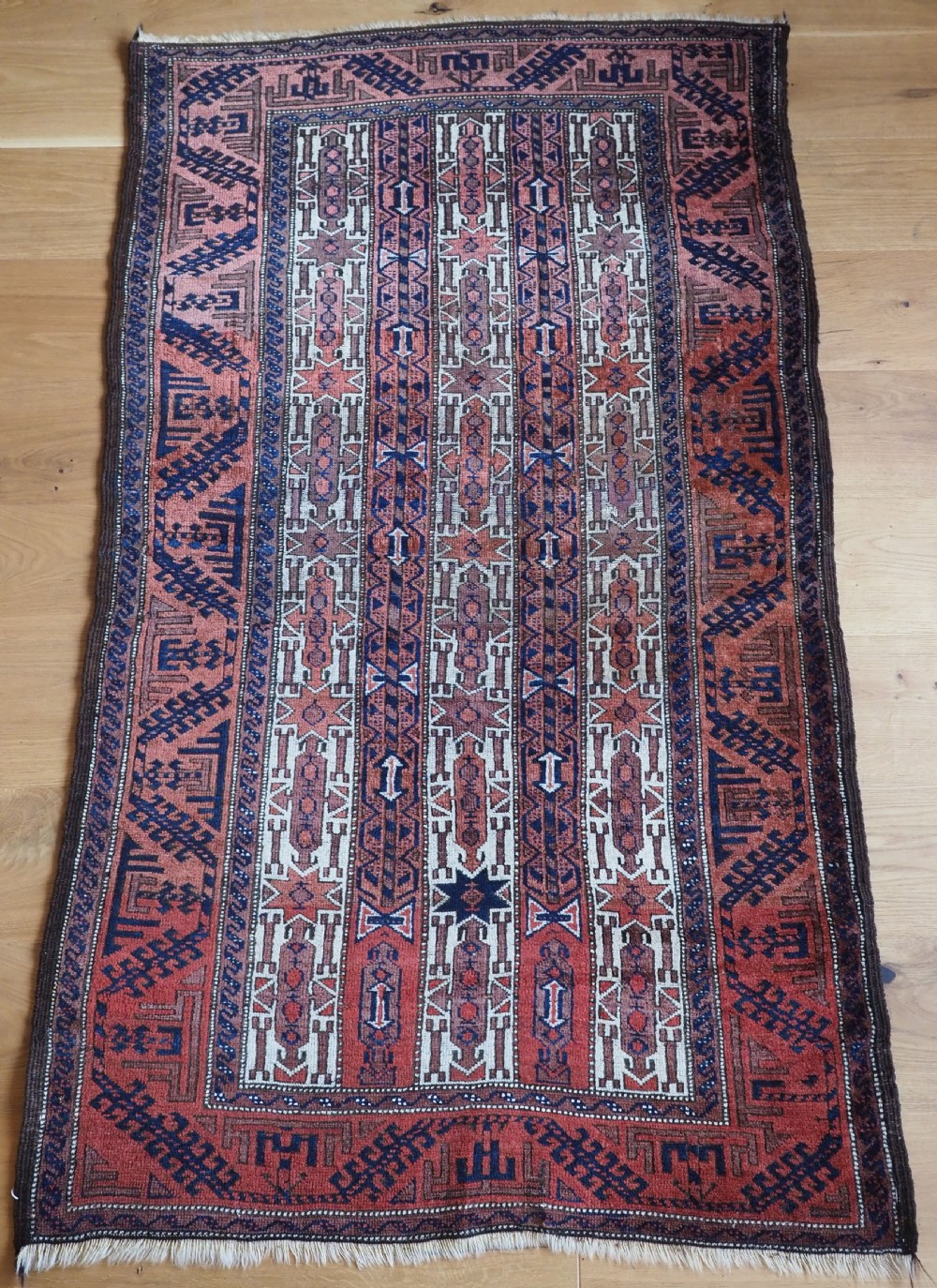 An antique hand-knotted Baluch wool rug featuring vertical stripe patterns in terracotta, navy blue, and white tones.