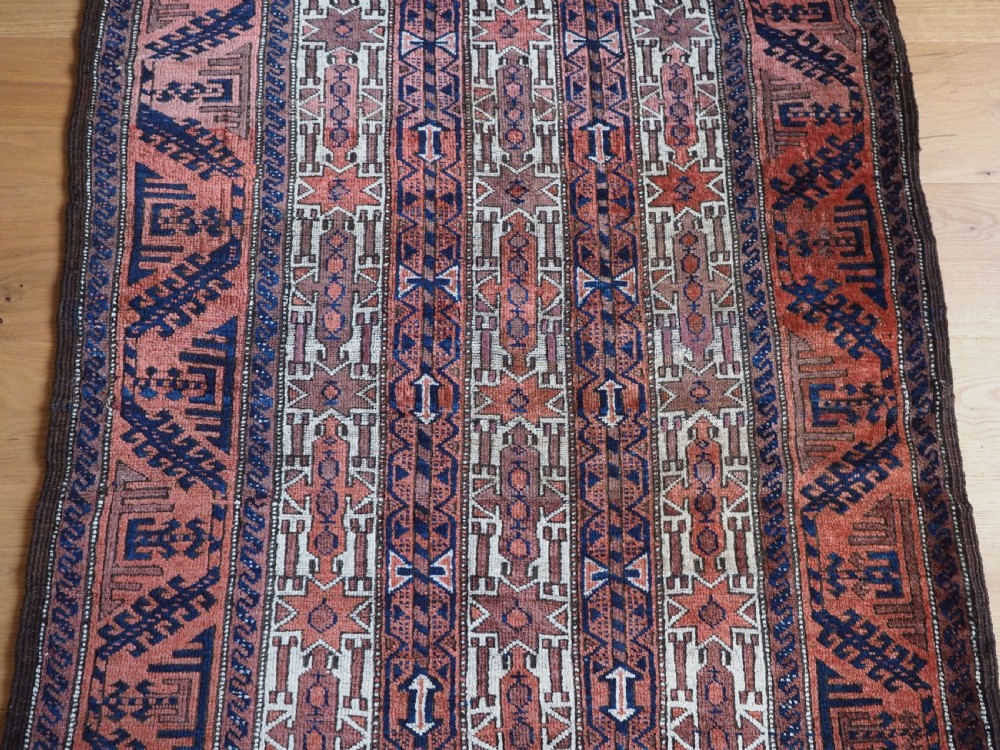 An antique hand-knotted Baluch wool rug featuring vertical stripe patterns in terracotta, navy blue, and white tones. View IV