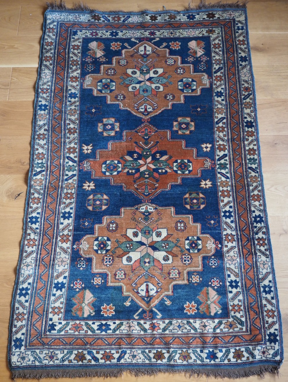An antique Caucasian Derbent hand-knotted wool rug featuring three stepped medallions on a deep blue field with geometric borders.