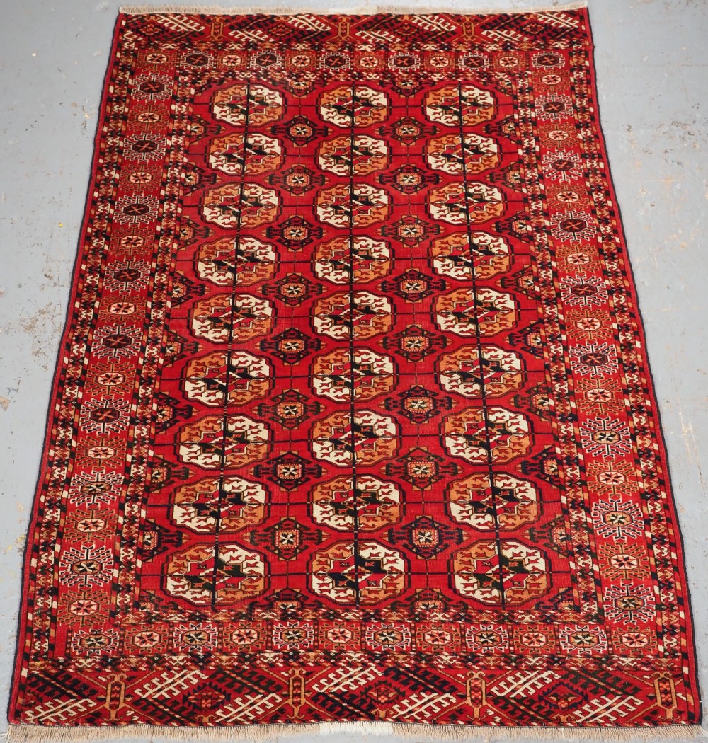 An antique rectangular hand-knotted Tekke Turkmen rug featuring repeating octagonal gol motifs on a deep red wool field framed by geometric borders.