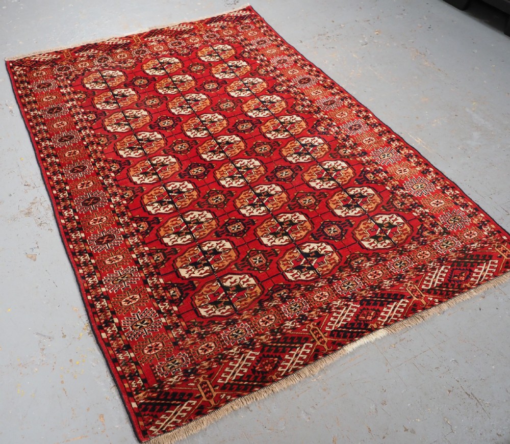 An antique rectangular hand-knotted Tekke Turkmen rug featuring repeating octagonal gol motifs on a deep red wool field framed by geometric borders. View II