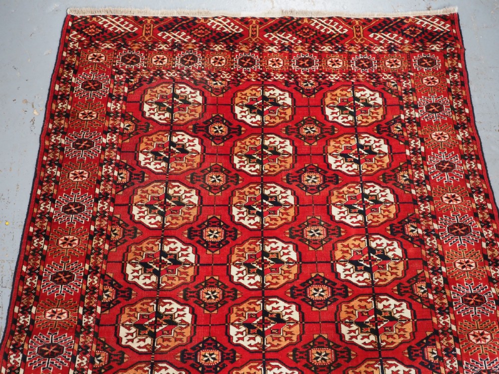 An antique rectangular hand-knotted Tekke Turkmen rug featuring repeating octagonal gol motifs on a deep red wool field framed by geometric borders. View III