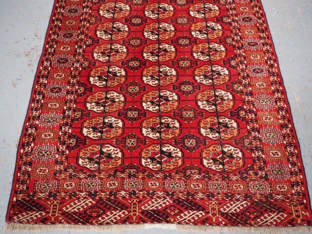 An antique rectangular hand-knotted Tekke Turkmen rug featuring repeating octagonal gol motifs on a deep red wool field framed by geometric borders. View IV