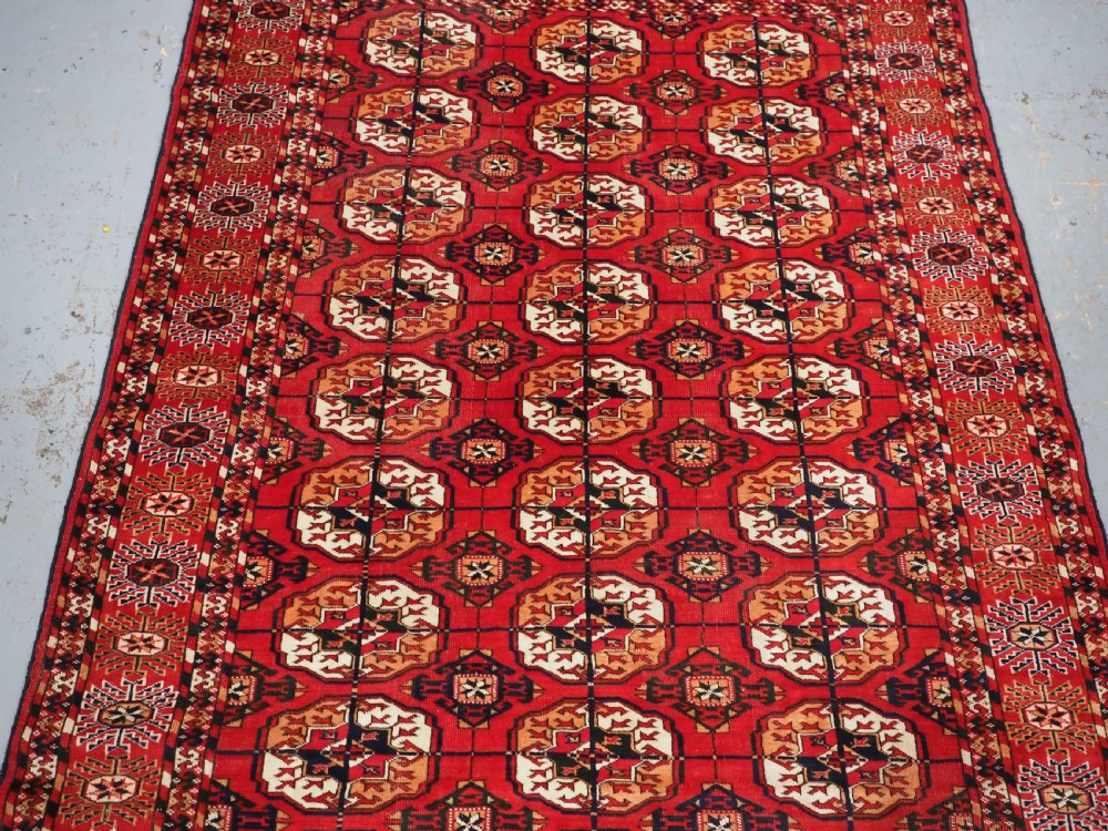 An antique rectangular hand-knotted Tekke Turkmen rug featuring repeating octagonal gol motifs on a deep red wool field framed by geometric borders. View V