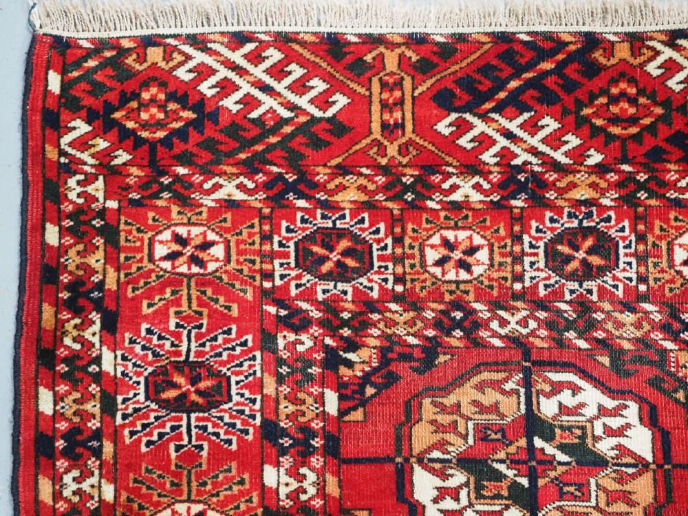 An antique rectangular hand-knotted Tekke Turkmen rug featuring repeating octagonal gol motifs on a deep red wool field framed by geometric borders. View VI