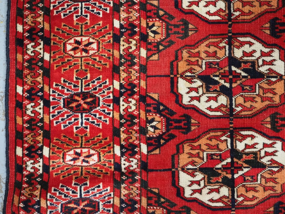 An antique rectangular hand-knotted Tekke Turkmen rug featuring repeating octagonal gol motifs on a deep red wool field framed by geometric borders. View VII