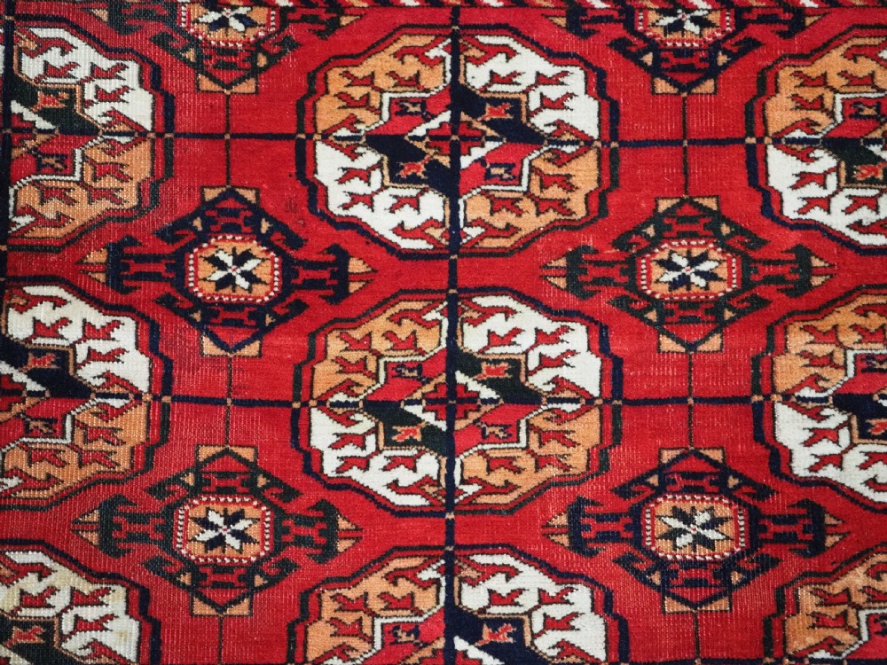 An antique rectangular hand-knotted Tekke Turkmen rug featuring repeating octagonal gol motifs on a deep red wool field framed by geometric borders. View VIII