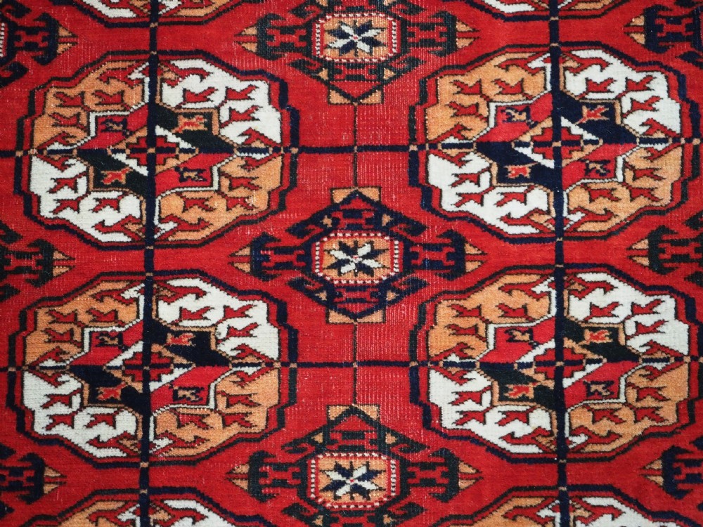 An antique rectangular hand-knotted Tekke Turkmen rug featuring repeating octagonal gol motifs on a deep red wool field framed by geometric borders. View IX