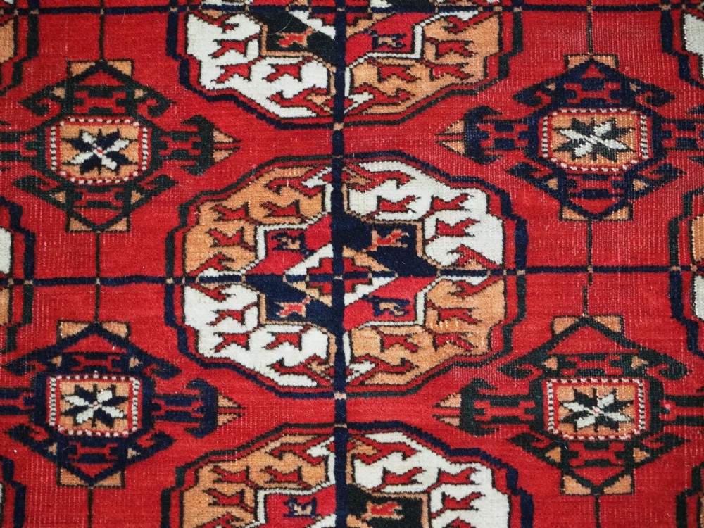 An antique rectangular hand-knotted Tekke Turkmen rug featuring repeating octagonal gol motifs on a deep red wool field framed by geometric borders. View X