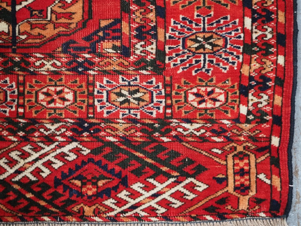 An antique rectangular hand-knotted Tekke Turkmen rug featuring repeating octagonal gol motifs on a deep red wool field framed by geometric borders. View XI