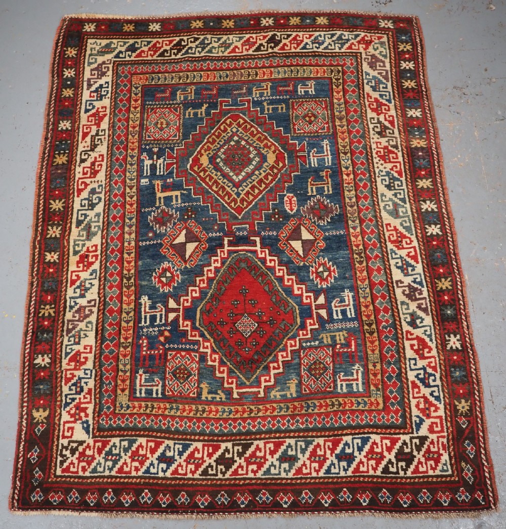 An antique Caucasian Bordjalou Kazak rug featuring a central navy blue field with two large red diamond medallions, zoomorphic animal motifs, and multi-layered geometric borders.