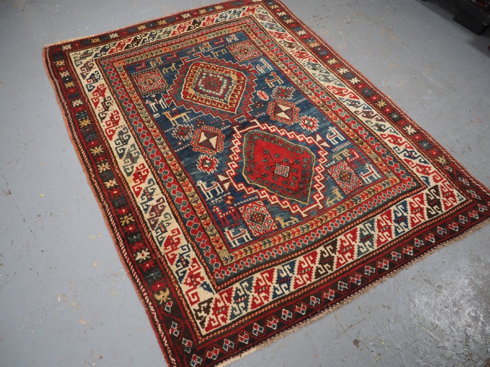 An antique Caucasian Bordjalou Kazak rug featuring a central navy blue field with two large red diamond medallions, zoomorphic animal motifs, and multi-layered geometric borders. View II