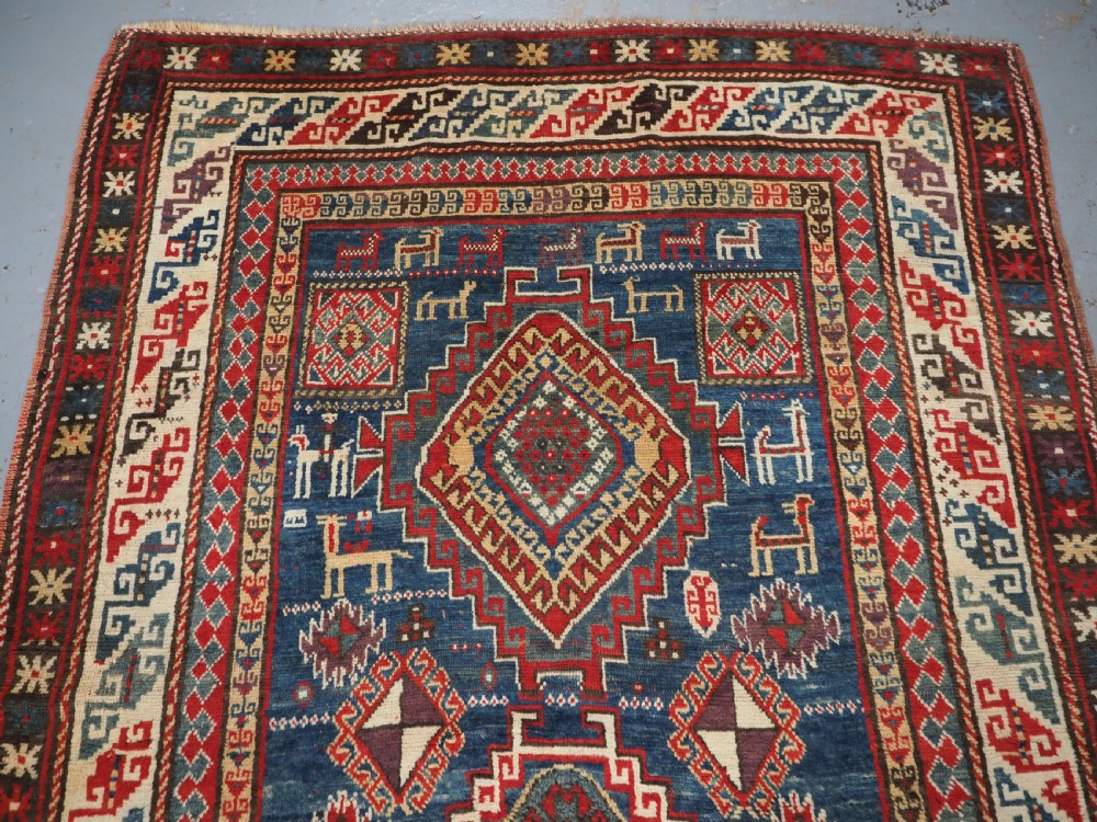 An antique Caucasian Bordjalou Kazak rug featuring a central navy blue field with two large red diamond medallions, zoomorphic animal motifs, and multi-layered geometric borders. View III