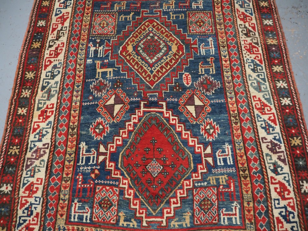 An antique Caucasian Bordjalou Kazak rug featuring a central navy blue field with two large red diamond medallions, zoomorphic animal motifs, and multi-layered geometric borders. View IV