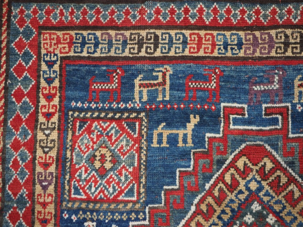 An antique Caucasian Bordjalou Kazak rug featuring a central navy blue field with two large red diamond medallions, zoomorphic animal motifs, and multi-layered geometric borders. View VIII