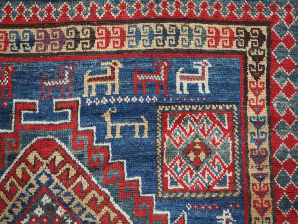 An antique Caucasian Bordjalou Kazak rug featuring a central navy blue field with two large red diamond medallions, zoomorphic animal motifs, and multi-layered geometric borders. View IX