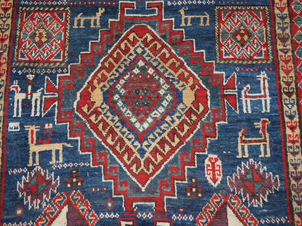 An antique Caucasian Bordjalou Kazak rug featuring a central navy blue field with two large red diamond medallions, zoomorphic animal motifs, and multi-layered geometric borders. View X