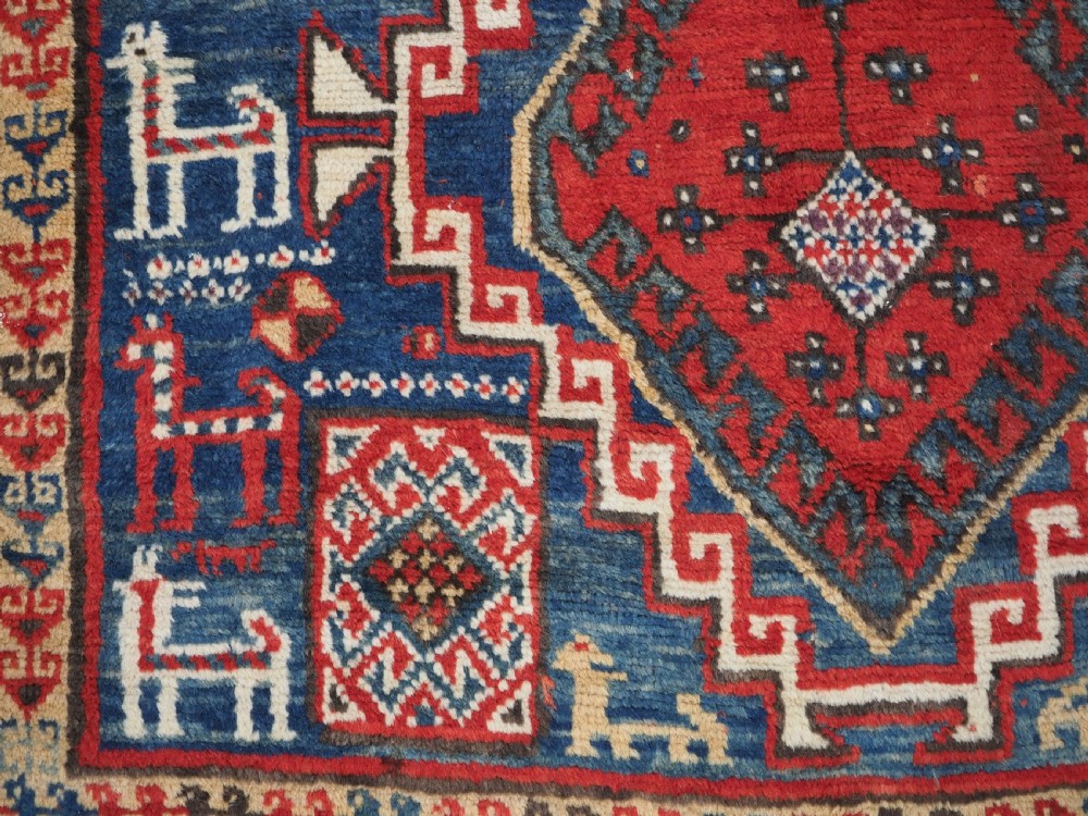 An antique Caucasian Bordjalou Kazak rug featuring a central navy blue field with two large red diamond medallions, zoomorphic animal motifs, and multi-layered geometric borders. View XII